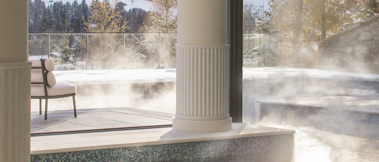 La piscine extérieure chauffée du Four Seasons Resort Megève fumant dans l'air froid, face aux pentes enneigées du Mont d'Arbois