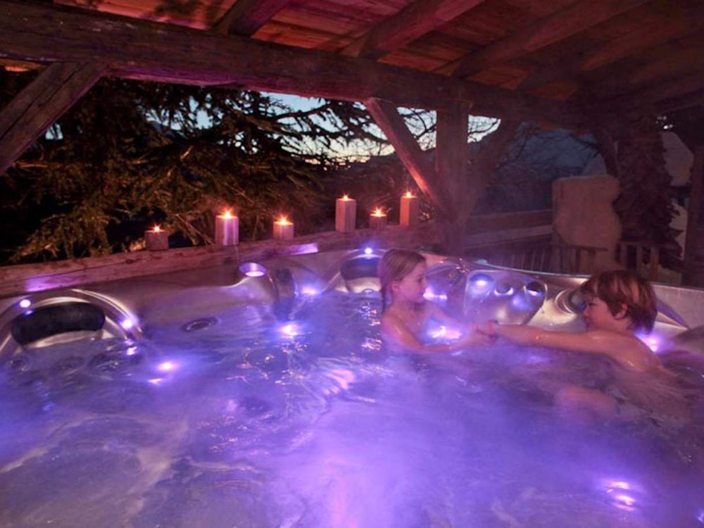 Le jacuzzi extérieur de la Croix Fry à la tombée du jour, sous la charpente, éclairé de bougies