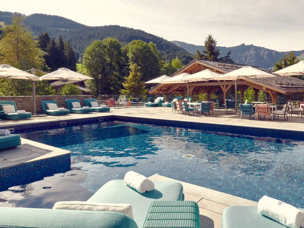 La piscine extérieure du Four Seasons Resort Megève l'été, ses transats et ses parasols face aux forêts