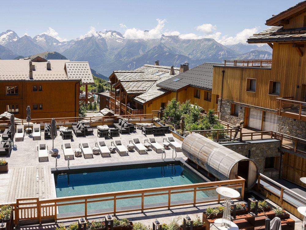 La piscine extérieure chauffée des Grandes Rousses, ses transats et le sauna tonneau, face aux sommets de l'Oisans