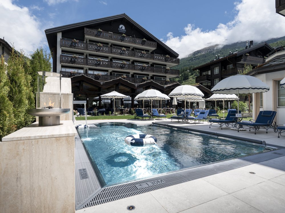La nouvelle piscine extérieure chauffée du Mirabeau à Zermatt, sa terrasse, ses parasols et le chalet de l'hôtel