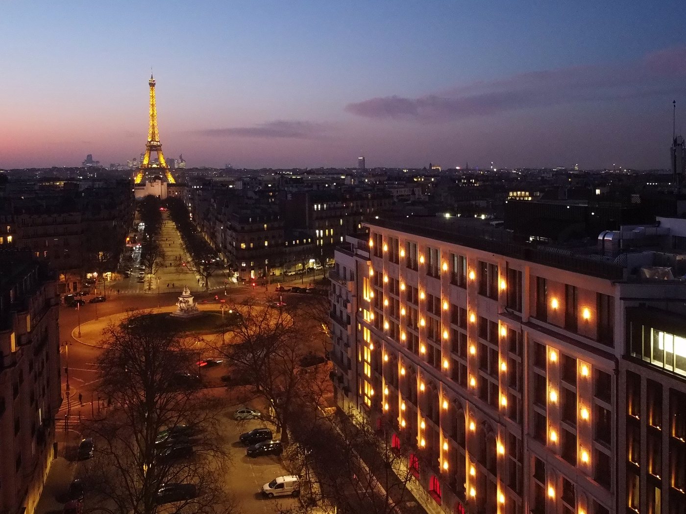 Le SAX Paris à la tombée de la nuit, avec la tour Eiffel illuminée à l'horizon
