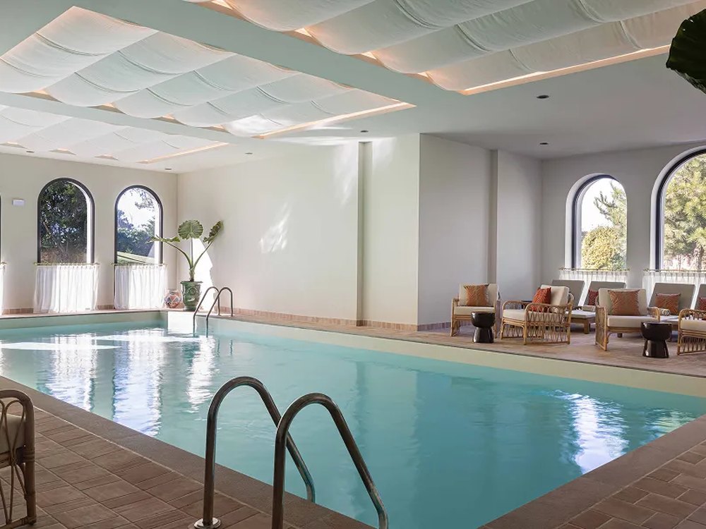 La piscine intérieure du spa de Maison Chiberta, sous un plafond voilé, avec ses fenêtres en arche et ses fauteuils