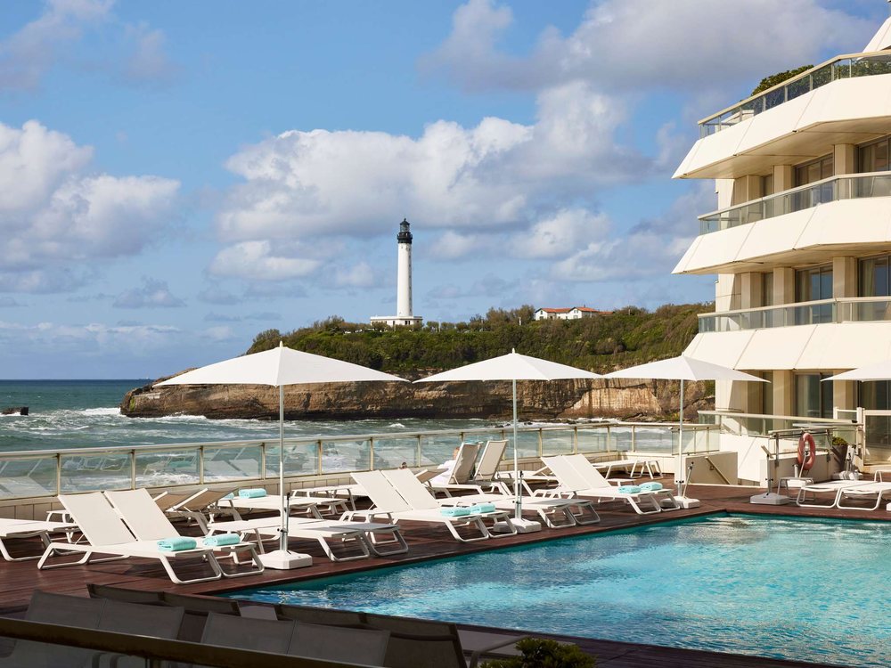 La piscine extérieure d'eau de mer du Sofitel Miramar, ses parasols blancs, la mer et le phare de Biarritz au fond