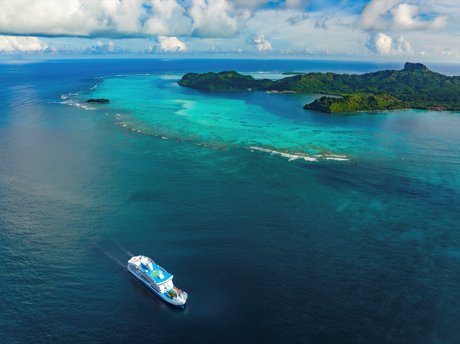 L'Aranui 5 vu du ciel, à l'approche d'une île haute et de sa barrière de corail en Polynésie française