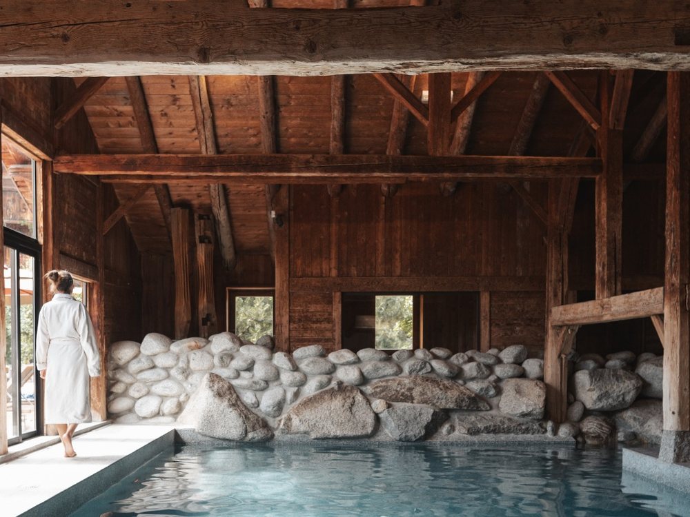 La piscine intérieure des Fermes de Marie, à Megève, entre charpente de vieux bois et rochers de granit