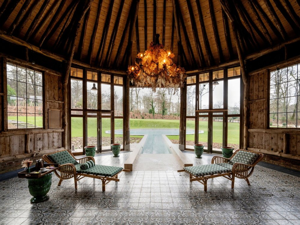 Le pool house du spa de l'Abbaye des Vaux-de-Cernay, sa charpente de bois et ses transats ouverts sur le parc