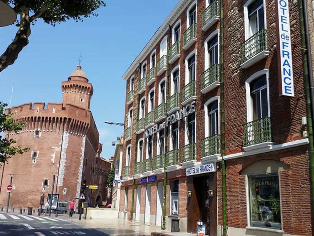 La façade de l'Hôtel de France sur le quai Sadi Carnot, avec le Castillet de brique rouge en arrière-plan