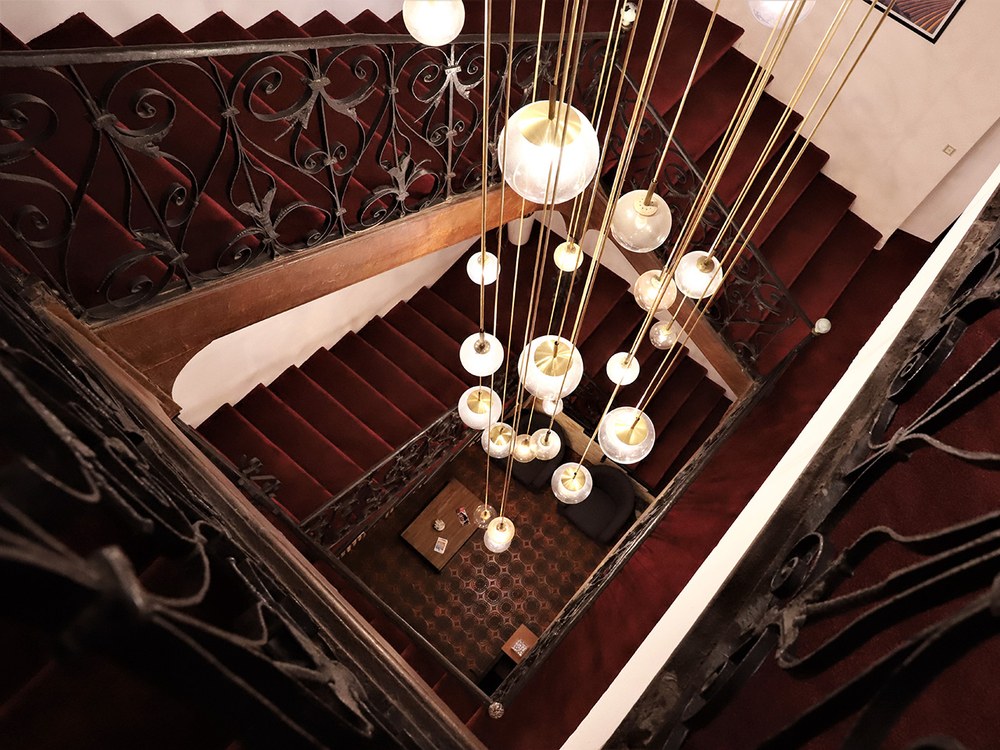 L'escalier monumental en fer forgé de l'Hôtel de la Loge, vu du haut, sous un lustre contemporain