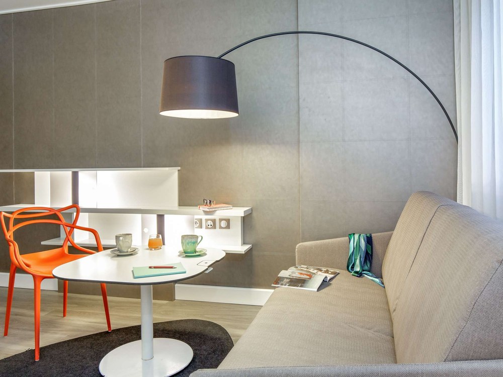 Le coin salon d'une suite du Novotel Suites Perpignan Centre, canapé, table ronde et grande lampe arc