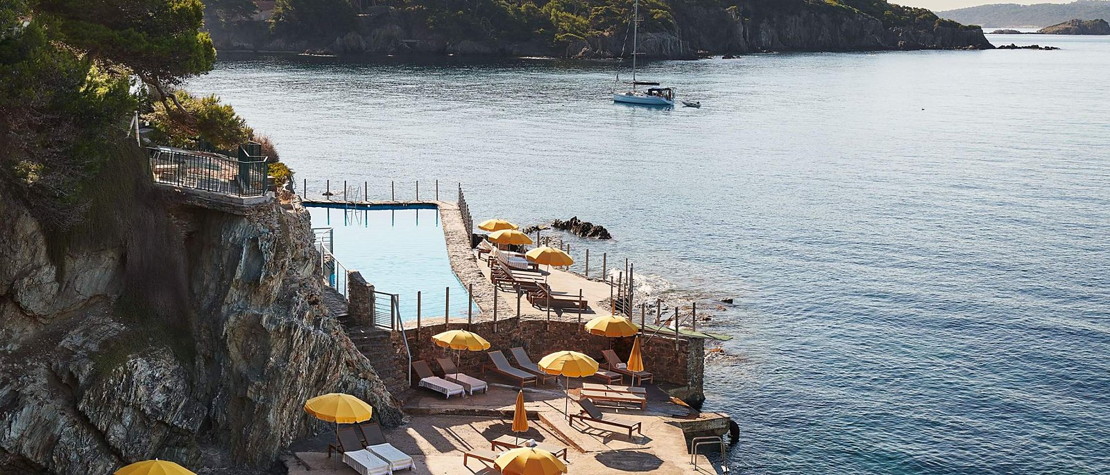 La piscine d'eau de mer du Provençal, creusée dans la roche au pied de la falaise, et ses parasols jaunes