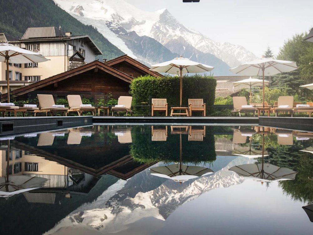La piscine extérieure chauffée du Hameau Albert 1er, ses transats et le massif du Mont-Blanc en fond