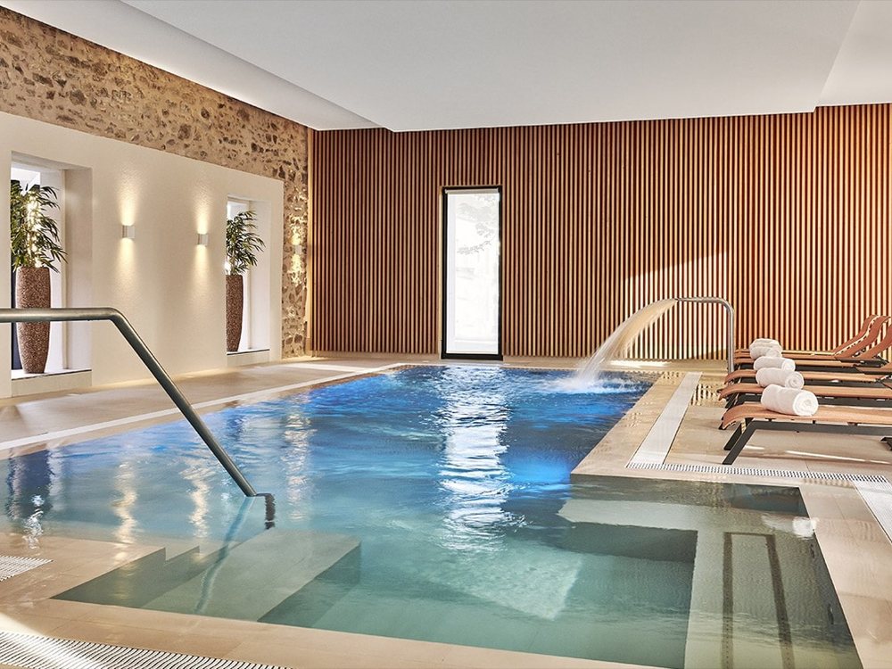 La piscine intérieure chauffée du spa du Château Saint-Jean, ses murs de pierre et son mur de bois clair