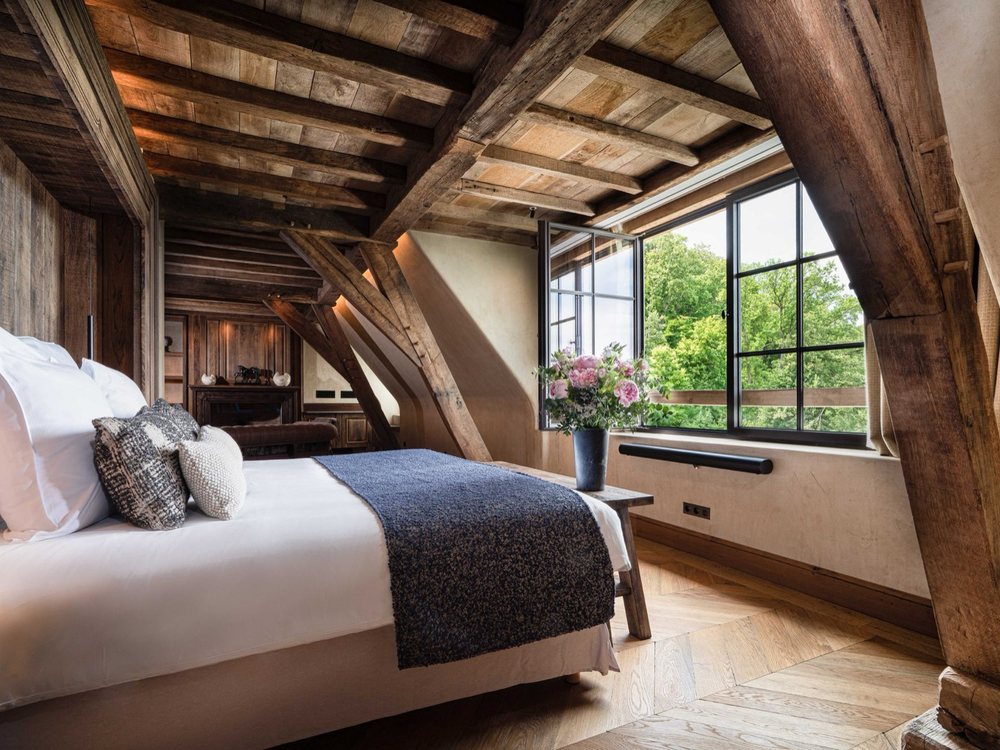 Une suite de La Ferme Saint-Siméon sous les poutres, son lit blanc et sa fenêtre ouverte sur le jardin