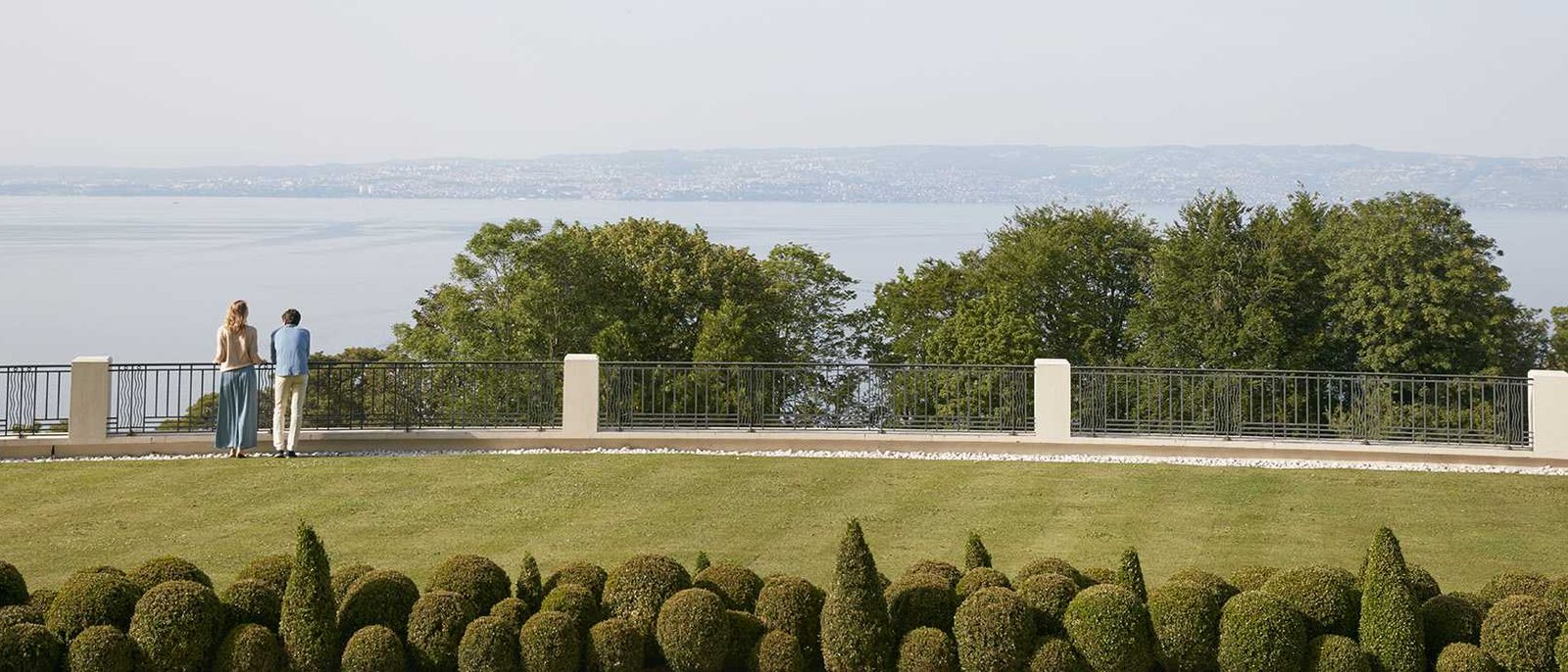 Une pelouse du parc de l'Hôtel Royal, ses buis taillés en boule et sa balustrade face au lac Léman