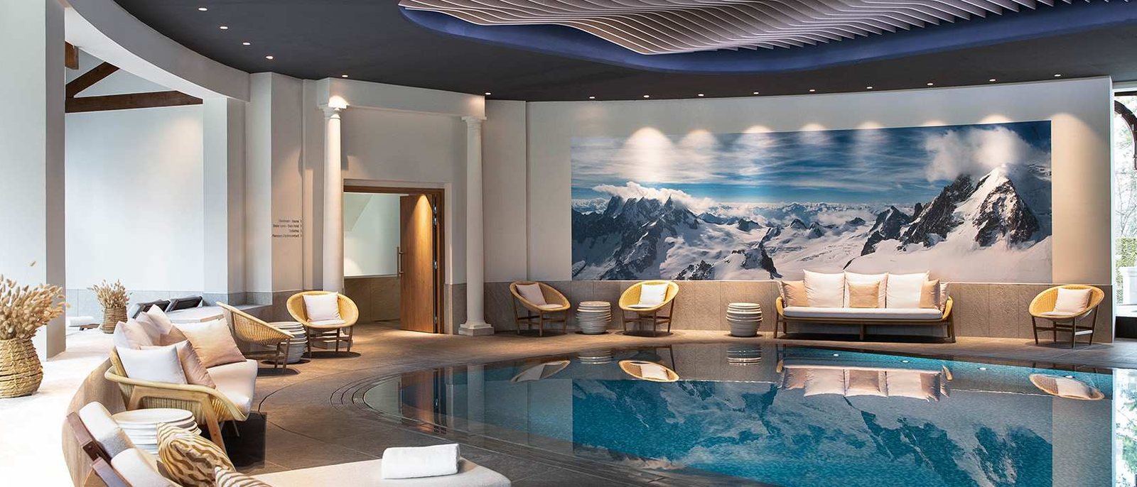 La piscine intérieure de l'evian®SPA de l'Hôtel Royal, ses canapés clairs et une grande fresque de sommets enneigés