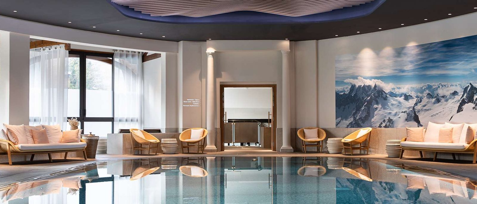 L'espace aquatique de l'evian®SPA, la piscine intérieure bordée de canapés et une fresque de montagnes enneigées