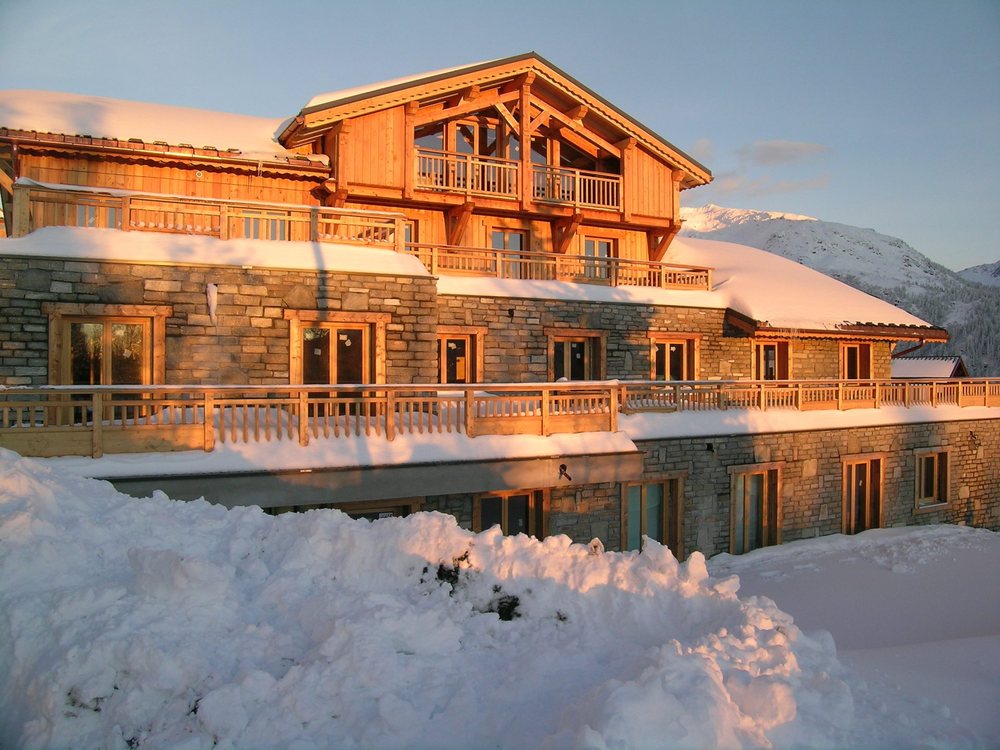 Le chalet de L'Accroche Cœur sous la neige, ses balcons de bois dorés par le soleil couchant