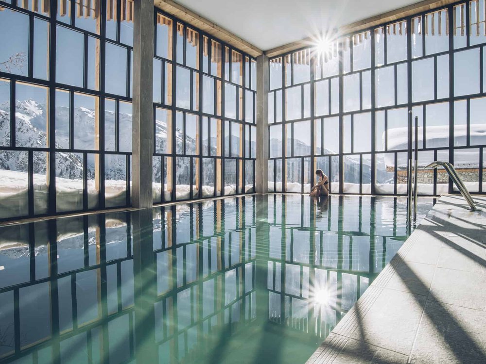 La piscine intérieure de l'Hôtel Alparena sous sa verrière, ses baies ouvertes sur les sommets enneigés