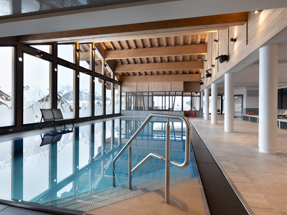 La piscine intérieure de l'Alpen Lodge, longée de grandes baies vitrées sur la neige et les sapins