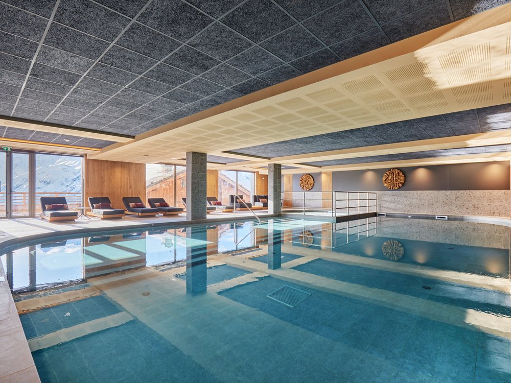 La piscine couverte chauffée de L'Écrin Blanc by Odalys, ses transats et ses baies sur la neige
