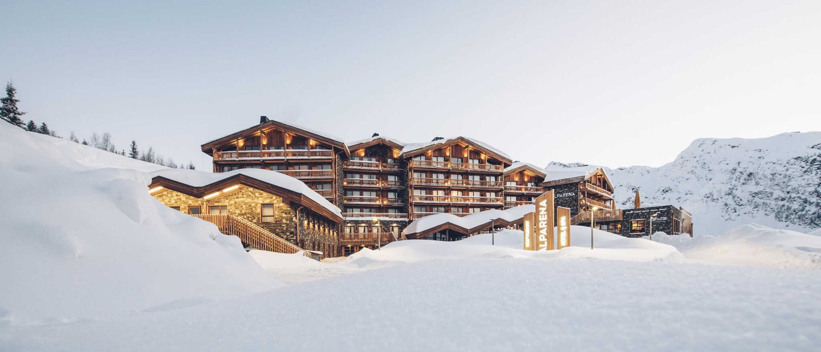 L'Hôtel Alparena sous la neige au crépuscule, ses chalets de bois et de pierre éclairés, aux Eucherts, à La Rosière