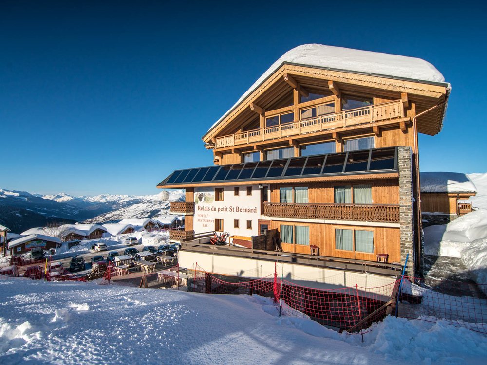 Le Relais du Petit Saint-Bernard sous la neige, sa façade de bois au-dessus de la station, ciel bleu