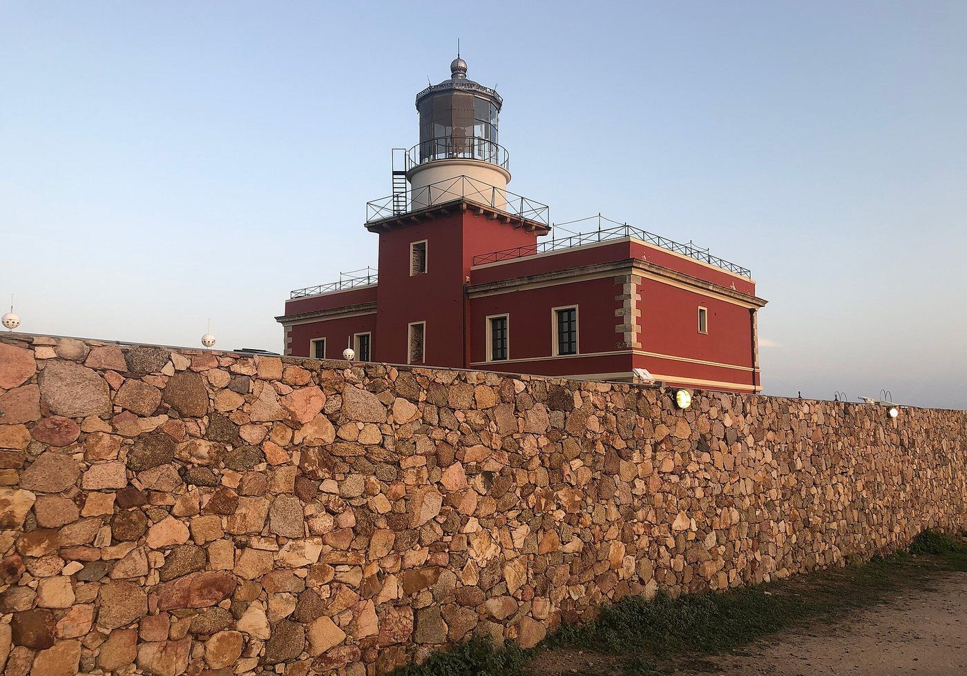 Le phare de Capo Spartivento, bâtiment rouge de 1856 derrière son mur de granit, à la pointe sud de la Sardaigne