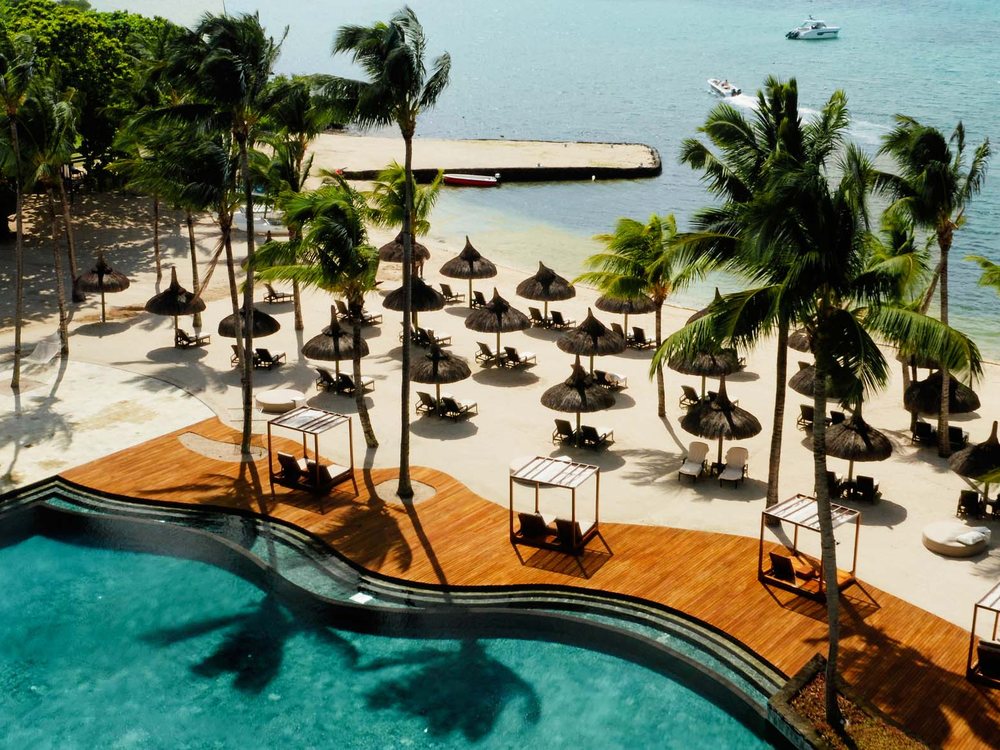 La piscine à débordement du Bay Club at Anahita, sa terrasse de bois et sa plage de parasols de chaume