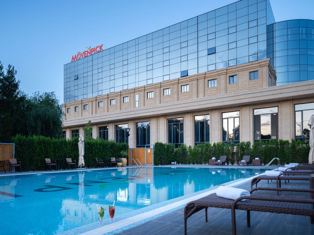 La piscine extérieure du Mövenpick Samarkand, devant la façade de pierre et de verre de l'hôtel