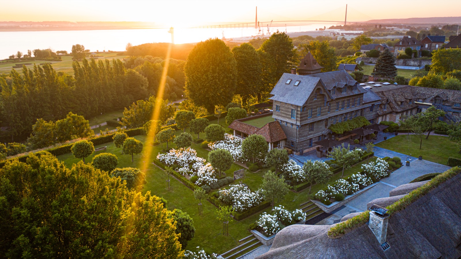 La Ferme Saint-Siméon vue du ciel, toits de chaume et bâtiments à colombages entourés de jardins, au-dessus de l'estuaire de la Seine
