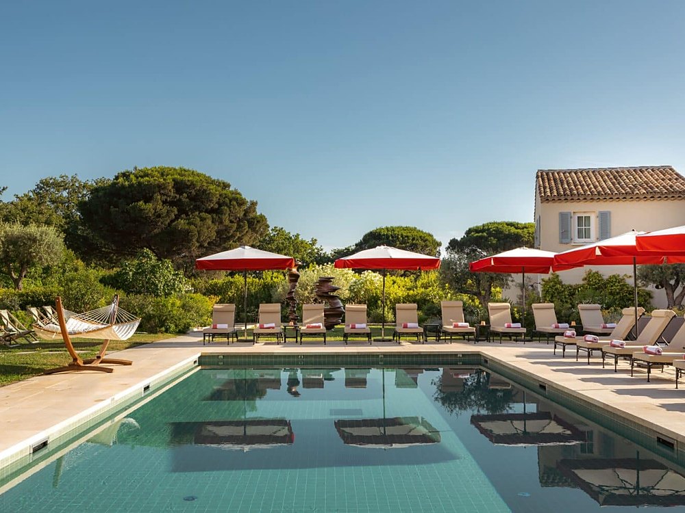 La piscine de Lou Pinet à Saint-Tropez, ses parasols rouges et sa pinède