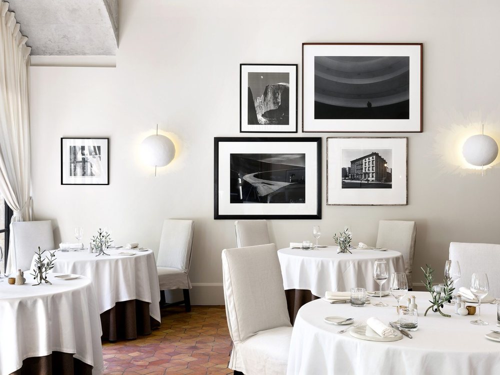 La salle de L'Oustau de Baumanière, tables rondes nappées de blanc et photographies en noir et blanc