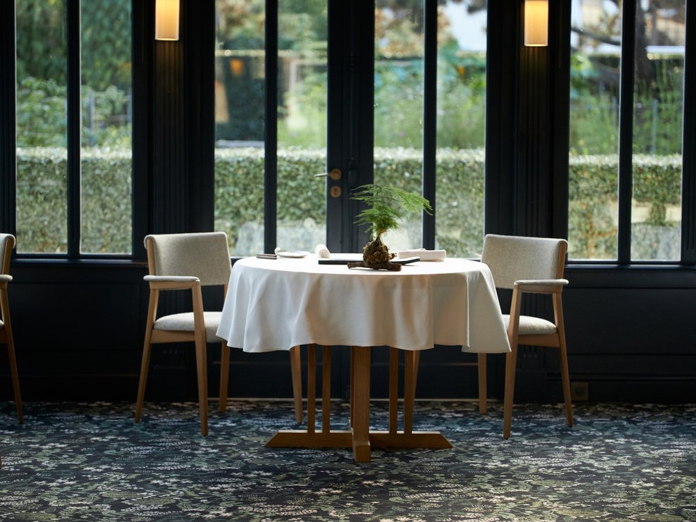 La salle de La Grand'Vigne aux Sources de Caudalie, table ronde nappée de blanc devant la verrière et les jardins