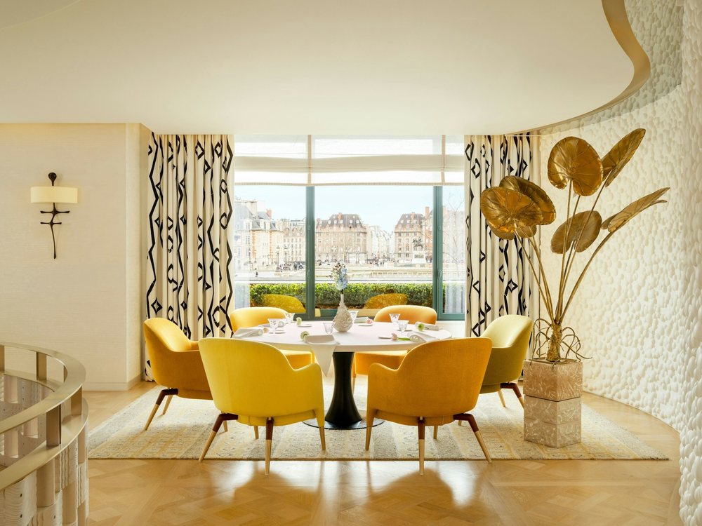 La salle de Plénitude au Cheval Blanc Paris, table ronde dressée, fauteuils jaunes et fenêtre sur la Seine