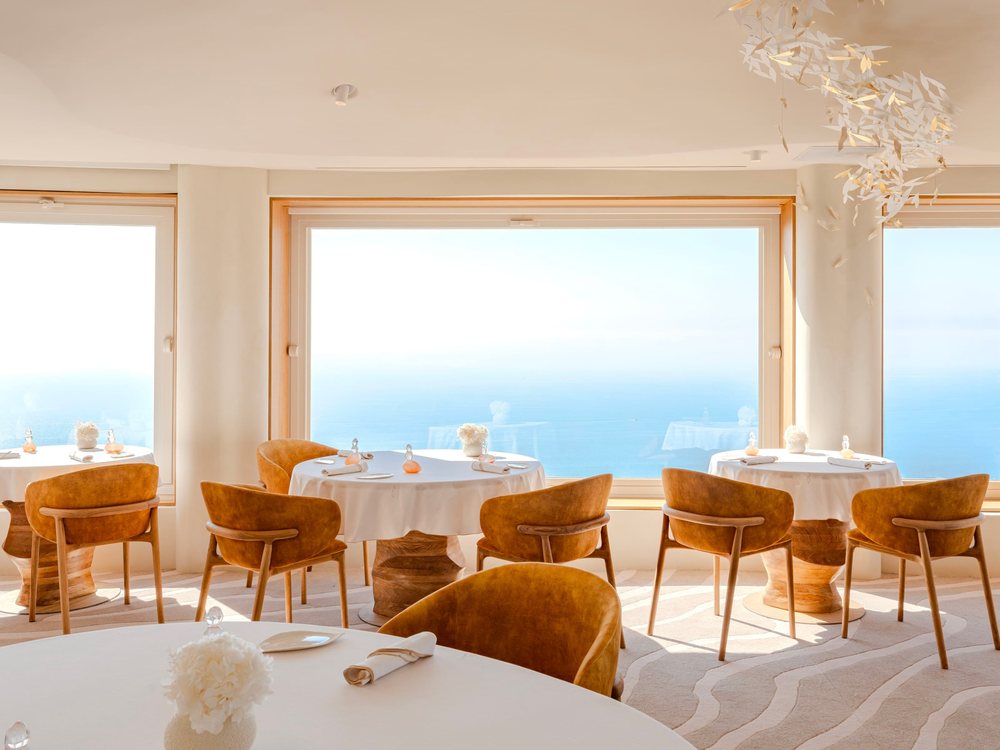 La salle rénovée du restaurant La Chèvre d'Or, tables dressées et grandes baies sur la Méditerranée