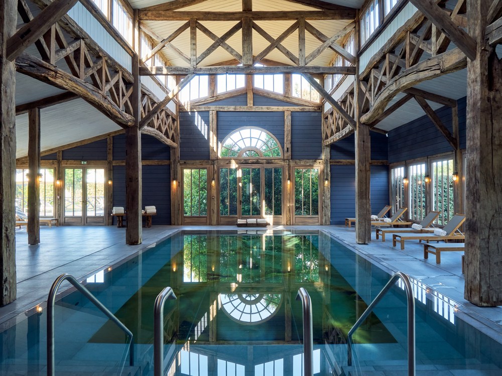 La piscine intérieure des Sources de Caudalie sous une charpente de bois, baies vitrées en demi-lune