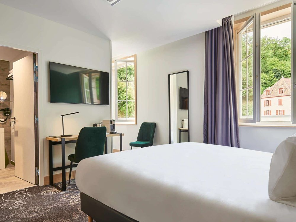 Une chambre claire du Grand Hôtel d'Évaux-les-Bains, sa fenêtre ouverte sur les arbres