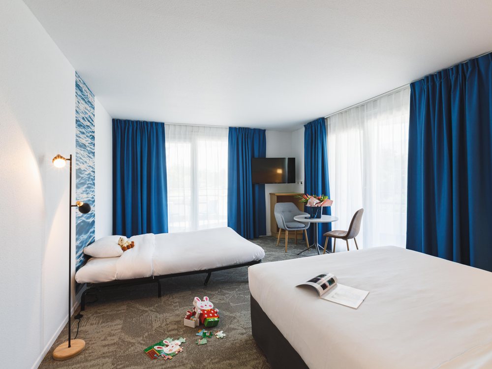Une chambre du Mercure Hôtel & Spa du Domaine de Marlioz, ses grands rideaux bleus et son coin salon