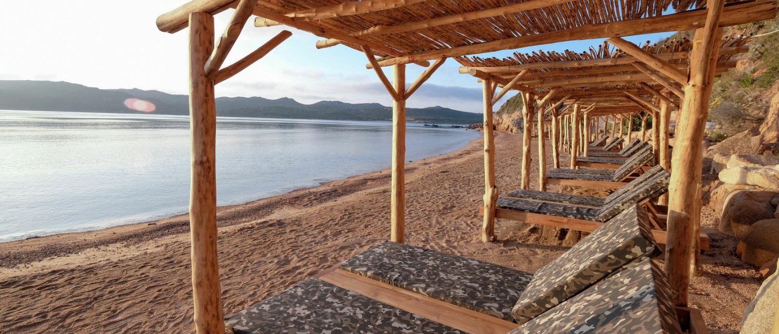 Une plage d'U Capu Biancu et ses lits à l'ombre de paillotes de bois, face au golfe de Sant'Amanza