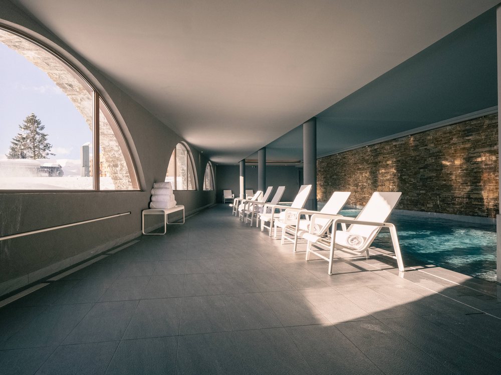 La piscine intérieure chauffée du Val Thorens, sous une grande baie en arc, ses transats blancs alignés