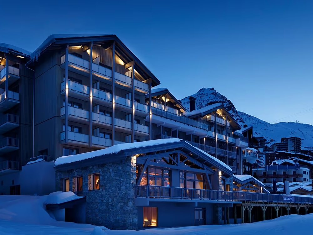 L'Hôtel Marielle à la nuit tombée, ses façades éclairées et ses toits couverts de neige face aux sommets