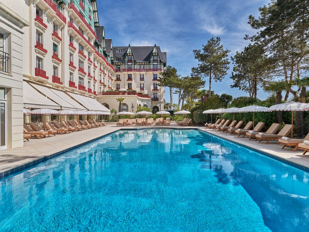 La piscine extérieure de L'Hermitage à La Baule, ses transats et la façade de l'hôtel sous le ciel bleu