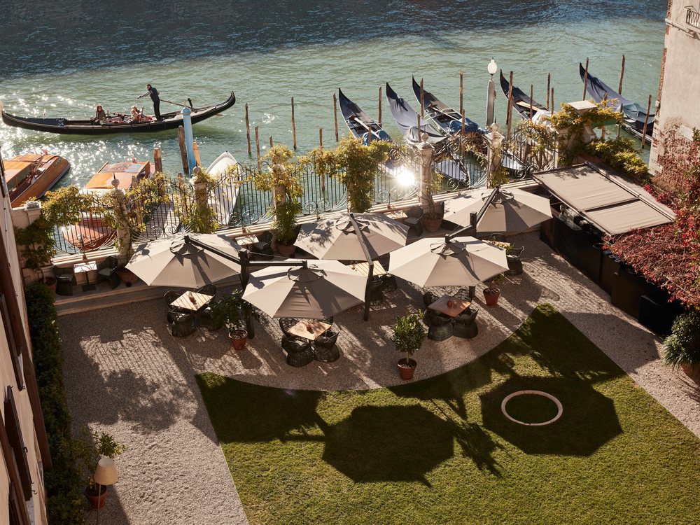 Le jardin d'Aman Venice au bord du Grand Canal, ses tables sous les parasols et les gondoles amarrées en contrebas