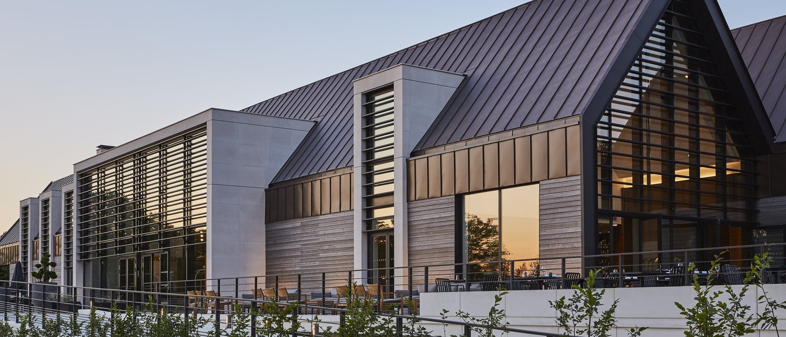 Les façades du Domaine des Vanneaux au crépuscule, leurs pignons de bois et de verre et leurs toits sombres en pente
