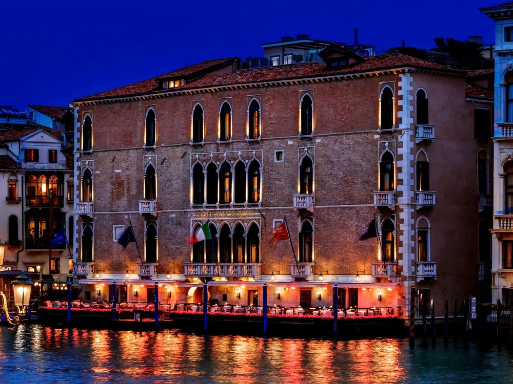 The Gritti Palace la nuit sur le Grand Canal, sa façade gothique rose éclairée et sa terrasse au bord de l'eau