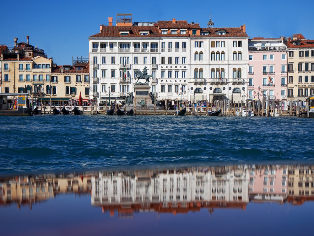 La façade blanche du Londra Palace sur la Riva degli Schiavoni, reflétée dans l'eau calme du bassin de Saint-Marc