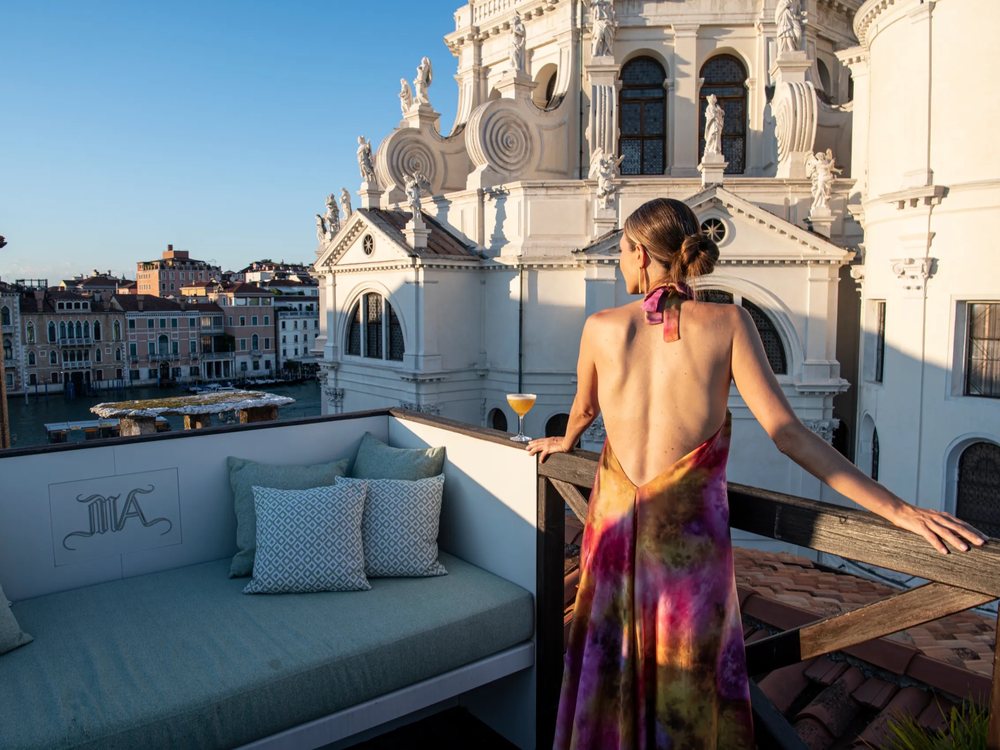 La terrasse de Ca' Maria Adele, son banc de coussins et une femme devant les coupoles de la Salute