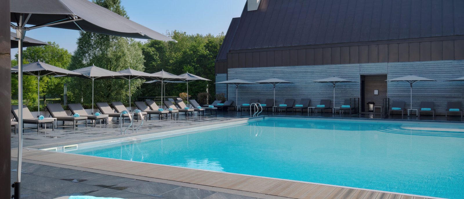 La piscine extérieure chauffée du Domaine des Vanneaux, ses transats et ses parasols gris, au pied d'un bâtiment au toit sombre
