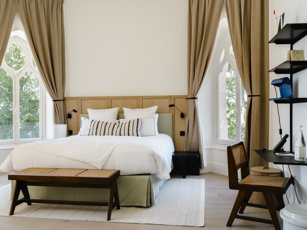 Une chambre des Hauts de Sancerre, lit blanc, banc de bois et hautes fenêtres voilées de lin